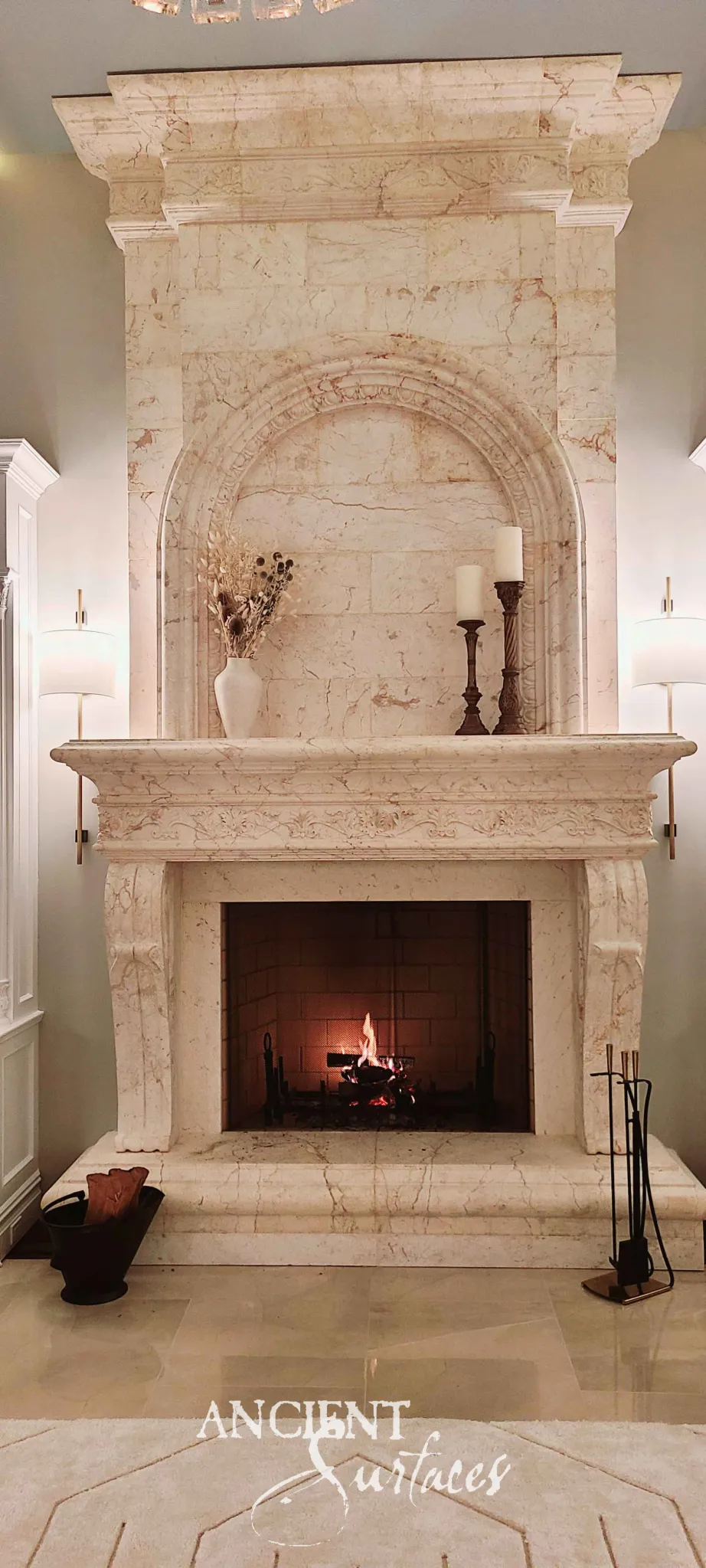 Reclaimed antique limestone mantel from Ancient Surfaces with a tall arched pediment and softly veined stone above a carved scroll corbel shelf