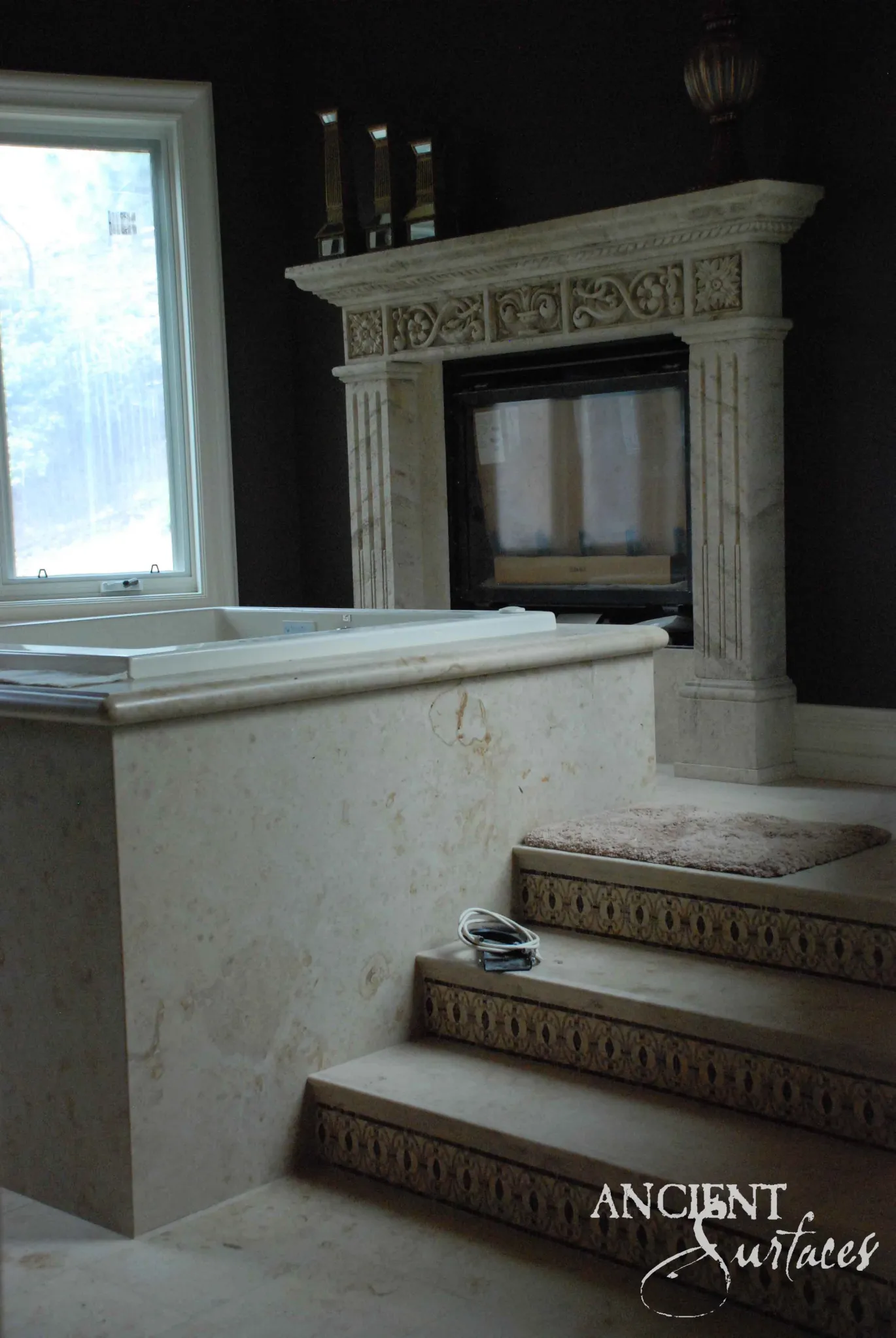 Reclaimed antique limestone mantel from Ancient Surfaces with an arcaded blind arch frieze and fluted pilasters beside a sunken tub in a private spa suite