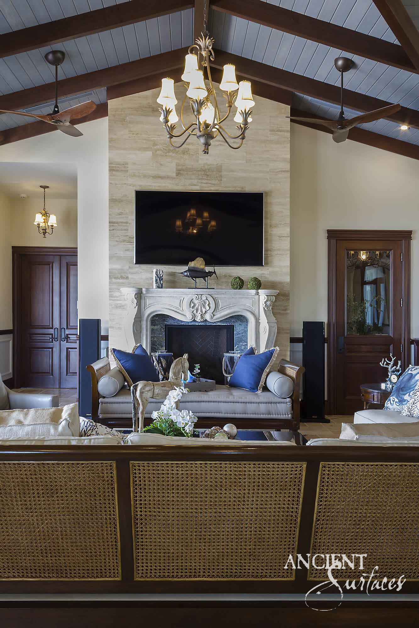 Reclaimed antique limestone fireplace from Ancient Surfaces clad floor to ceiling in a vaulted wood beamed great room with a carved shell cartouche mantel line